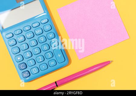 Flat lay of Calculator, pen and blank sticky note on yellow background. Vibrant colors Mock up Stock Photo