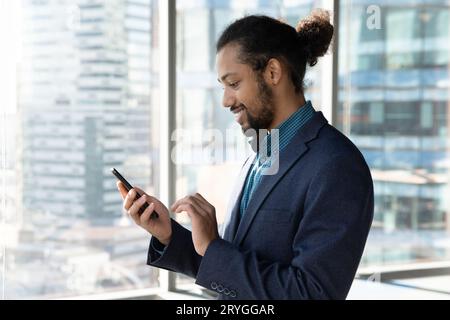 Side view African American businessman using smartphone, standing near window Stock Photo