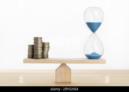 Time and money balance concept. Sand clock and stacked coins on Seesaw Stock Photo