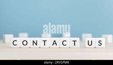 Contact us message on cube blocks on wood table. Copy space. Blue background Stock Photo