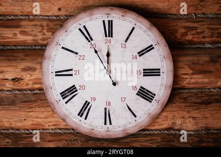Round vintage clock showing five minutes to noon, midnight hangs on wooden wall. Decorative elements. Countdown. Design. Cozy house . Retro style. Sen Stock Photo