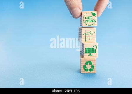 Net Zero and Carbon Neutral Concept. Hand putting wood block with Net Zero icon on top of others with green energy icons. Blue b Stock Photo