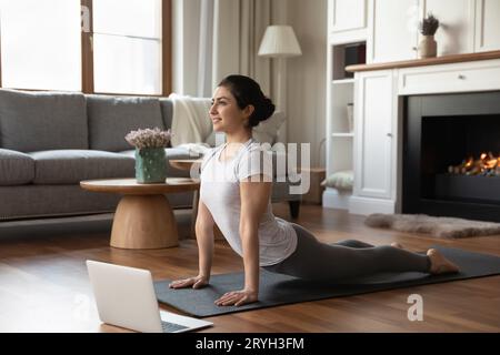 Smiling Indian woman practicing yoga online, working out at home Stock Photo