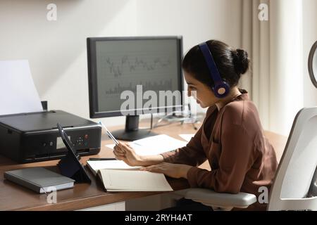 Indian woman in headphones taking notes, using tablet, studying online Stock Photo