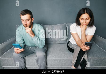 Bored young couple sitting on couch and looking at their smart phones Stock Photo