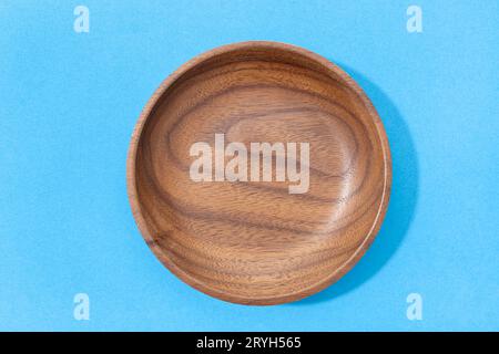 Empty round wooden plate or bowl isolated on blue background. Walnut wood. Top view Stock Photo