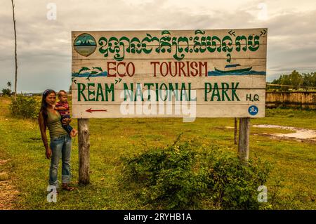A cute Cambodian mother stands w/ her mixed race son near the 'Ream National Park' hand painted sign. Preah Sihanouk province, Cambodia. © Kraig Lieb Stock Photo