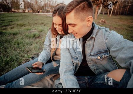 A young fashionable couple of students smiles while looking at the phone in the park Stock Photo