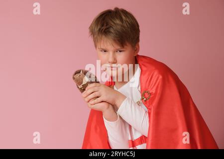 Little boy dressed like superhero holding a toy on pink background Stock Photo