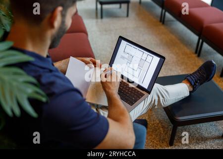 Close up of male architect is making notes in note pad during work on laptop in coworking space Stock Photo