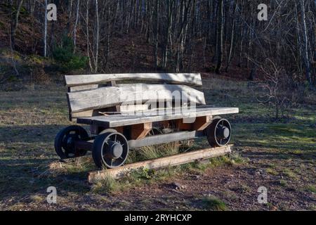 Wooden bench on the wheels from an old mining cart on a rail track. Decoration in the park. Stock Photo