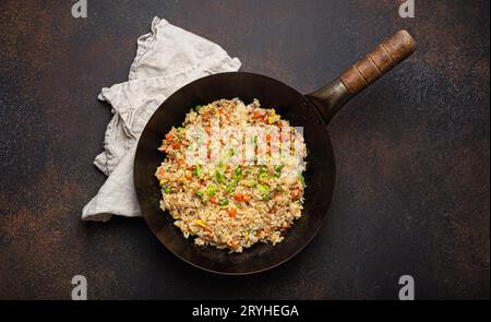 Authentic Chinese and Asian fried rice with egg and vegetables in wok top view, rustic concrete table background. Traditional di Stock Photo