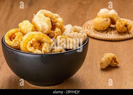 Closeup view of homemade crispy deep fried pork rinds in black ceramic bowl and on bamboo mat . Stock Photo