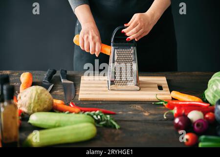 Woman cooking in kitchen at home, rubs carrots on a grater Stock Photo