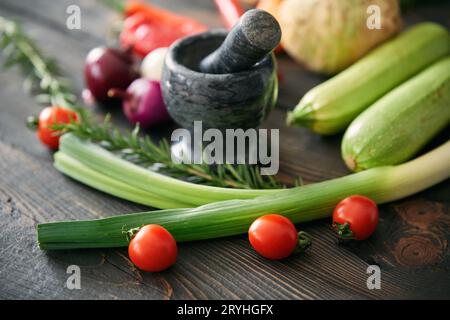 Background with assorted raw organic vegetables and black marble mortar with a pestle on wooden kitchen table Stock Photo