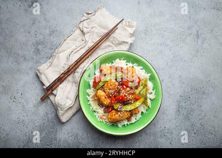 Asian sweet and sour sticky chicken with vegetables stir-fry and rice in ceramic bowl with chopsticks top view, gray rustic ston Stock Photo