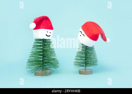 Two small Christmas trees in red Santa Hats. Decorating of Artificial Fir tree. Beautiful imitation of a mini Christmas tree, with Santa Cap on blue b Stock Photo