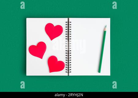 Notebook with pencil, red hearts. Open notebook on green emerald color background, spiral notepad. Top view. Notepad with blank white page for write, Stock Photo