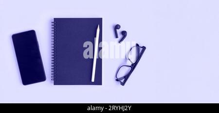 Notebook with pencil, glasses, phone and headphones. Open notebook on purple background, spiral notepad. Top view. Notepad with blank black pages for Stock Photo