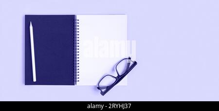 Notebook with pencil, glasses. Open notebook on purple color background, spiral notepad. Top view. Notepad with blank white and black pages for write, Stock Photo