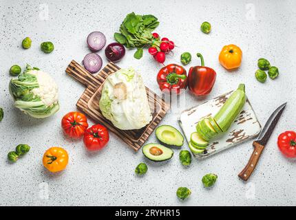 Fresh various vegetables with wooden cutting boards and knife on white kitchen table top view. Cooking vegetarian meal from heal Stock Photo