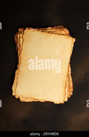 Close up stack of several blank old antique vintage brown paper parchment sheets with aged and weathered edges over dark table b Stock Photo