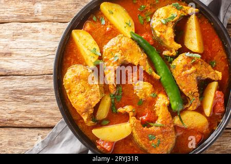 Machher jhol or machha jhola, is a traditional spicy fish curry in Bengali and Odia cuisines closeup on the plate on the wooden table. Horizontal top Stock Photo