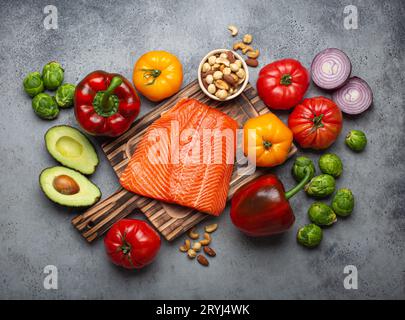Fresh raw salmon fillet on wooden cutting board, organic bio vegetables and nuts, rustic stone grey background top view. Ingredi Stock Photo