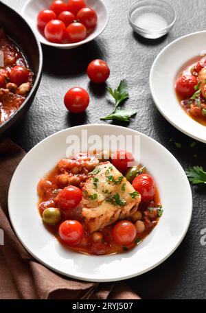 Cod stew with chickpeas, cherry tomatoes and olives on plate over dark stone background. Stock Photo