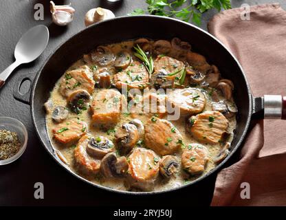 Pork medallions with mushroom gravy in cast iron pan over dark stone background. Close up view Stock Photo