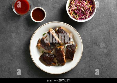 Pork ribs with sauce and vegetable salad over dark stone background. Top view, flat lay Stock Photo