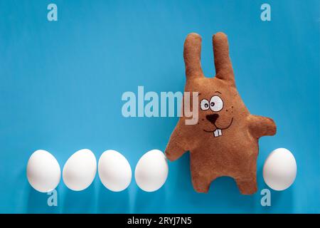 Easter hunt with toy bunny and colored eggs in glass on blue background Stock Photo
