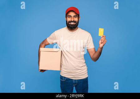 Easy payment. Indian male courier in uniform holding credit card and cardboard parcel box, carrying package Stock Photo