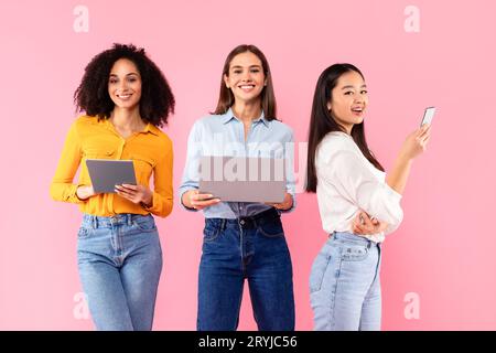 People and technology concept. Happy diverse female friends using different gadgets laptop, tablet and smartphone Stock Photo