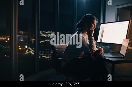 businesswoman working late in her home office, focusing on a digital marketing project. Woman putting in long hours into her work, sitting with a lapt Stock Photo