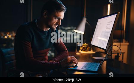 Caucasian businessman works from his home office, typing on a laptop late into the night. Dedicated and productive, he navigates deadlines and manage Stock Photo