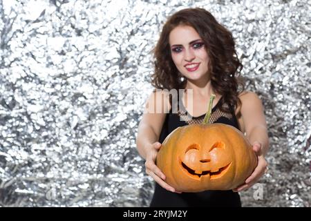 Pretty woman with bright make up, giving pumpkin to camera. Stock Photo