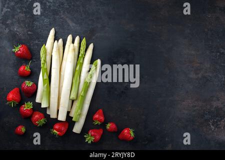 Ripe red strawberries and white asparagus from organic farming offered as top view on a rustic black board with copy space on ri Stock Photo