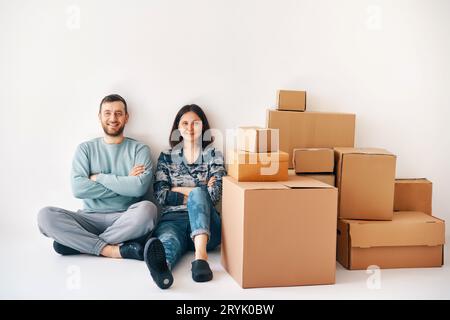 Smiling happy couple sitting on floor after the moving to new house with cardboard boxes Stock Photo