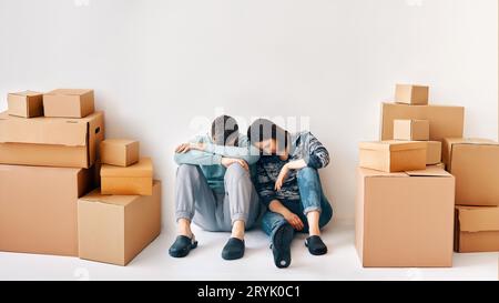 Young couple fell asleep after a moving day sitting on the floor surrounded by cardboard boxes Stock Photo