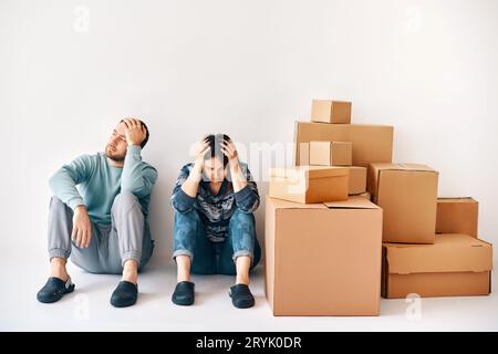 Young couple fell asleep after a moving day sitting on the floor surrounded by cardboard boxes Stock Photo