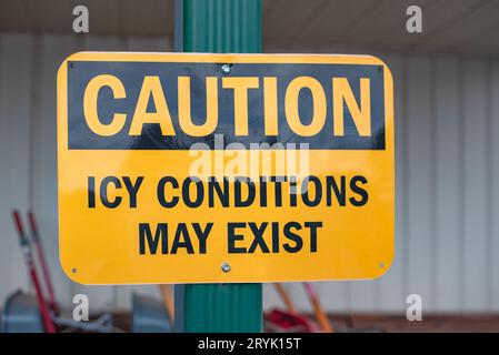 Yellow and black sign in front of a business warns, Caution, Icy Conditions May Exist. Stock Photo