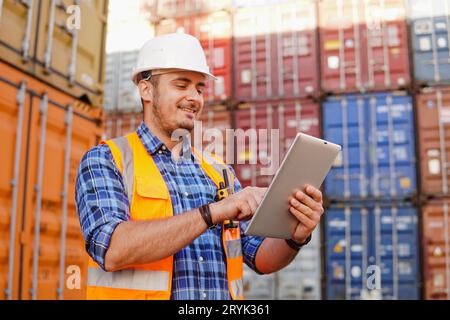 Container warehouse worker in uniform uses a digital tablet to inspect inventory in a large container yard. Logistics and export of business. Stock Photo