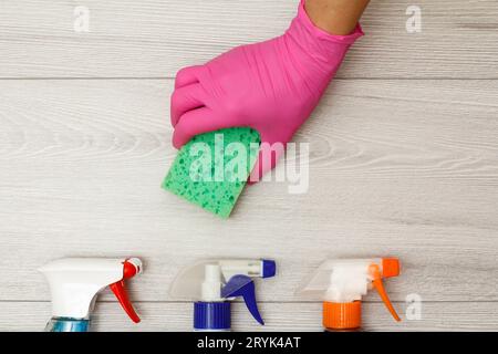 Hand in a rubber glove holding the sponge with the bottles of detergent. Stock Photo