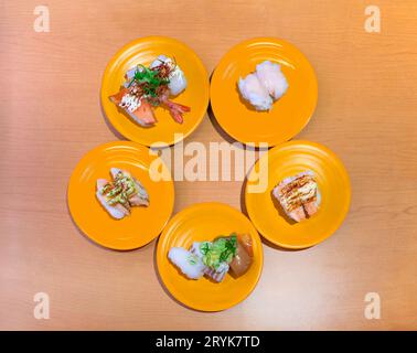 Overhead angle photography of an assortment of nigiri-zushi or sushi on five yellow plates arranged in circle on the table of a Kaiten-zushi eatery Stock Photo