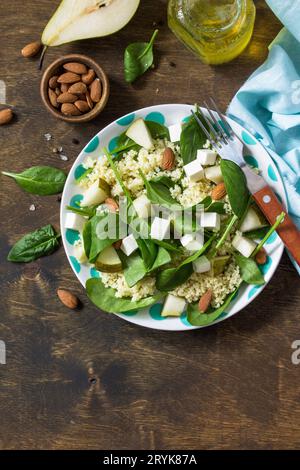 Autumn fruit salad. Couscous salad with pear, spinach, feta cheese and vinaigrette sauce on a wooden rustic table. Top view flat Stock Photo