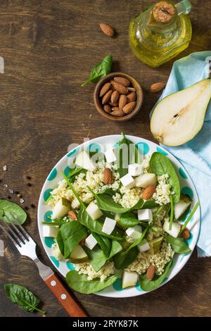 Autumn fruit salad. Couscous salad with pear, spinach, feta cheese and vinaigrette sauce on a wooden rustic table. Top view flat Stock Photo