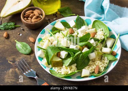 Autumn fruit salad. Couscous salad with pear, spinach, feta cheese and vinaigrette sauce on a wooden rustic table. Stock Photo