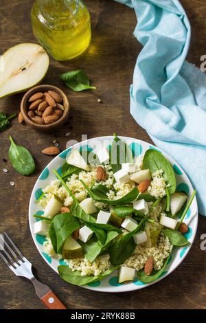 Autumn fruit salad. Couscous salad with pear, spinach, feta cheese and vinaigrette sauce on a wooden rustic table. Stock Photo