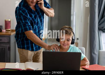 Midsection of caucasian grandfather touching shoulder of grandson doing homework over laptop Stock Photo